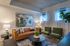 Elegant living room with modern artwork, stylish leather sofa, cozy green chairs, and lush indoor plant, illuminated by natural light through large windows.