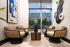 Chic apartment lounge featuring stylish beige chairs, modern art, and expansive windows overlooking a vibrant urban streetscape.