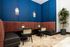 Inviting seating area with modern decor, featuring cozy brown leather booths, chic tables, and vibrant blue walls adorned with elegant lighting fixtures. Ideal for relaxation in style.