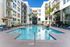 Luxurious apartment complex featuring a sparkling outdoor pool, surrounded by modern lounge chairs and shaded seating areas.