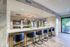 Modern kitchen with elegant marble countertops, stylish pendant lighting, and sleek bar stools facing a cozy open-plan layout with greenery.