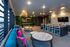 Modern lounge area with chic decor, vibrant pink and teal cushions, illuminated wall sign, and sleek bar seating.