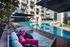 Luxurious apartment complex with a stunning outdoor pool area, featuring stylish sun loungers and vibrant seating under large umbrellas.