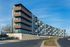 Modern apartment complex with panoramic balconies, elegant architecture, and tree-lined street in vibrant city area.