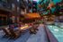 Chic outdoor apartment courtyard with stylish fire pit, cozy seating, vibrant wall mural, and elegant lighting, adjacent to a tranquil water feature.