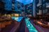 Luxurious apartment complex showcasing a vibrant evening poolside ambiance with sparkling fountains, cozy lounge chairs, and a modern fire pit, ideal for relaxation.