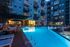 Inviting apartment complex courtyard with a luxurious, illuminated swimming pool, modern lounge chairs, and vibrant evening ambiance.