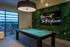 Chic recreation room with a pool table, vibrant greenery wall, and an inviting neon sign reading 'this must be the place', offering a stylish and relaxing ambiance.