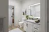 Modern bathroom with sleek white cabinetry, elegant mirror lighting, glass-enclosed shower, and stylish decor.