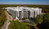 Modern multi-story apartment building surrounded by lush greenery and a spacious parking lot, offering luxury living with scenic views.