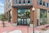 Modern building exterior with large glass windows and brick facade, featuring prominent leasing office entrance.