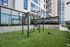 Modern outdoor gym with workout equipment on green turf, surrounded by vibrant high-rise buildings and reflecting windows.