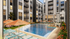 Luxury apartment complex featuring a stunning outdoor pool area with stylish lounge chairs and vibrant umbrellas, surrounded by modern multi-story buildings and lush landscaping.
