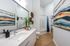 Modern bathroom featuring a sleek vanity with a large mirror, vibrant abstract art, and elegant wood flooring.
