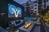 Chic apartment courtyard featuring a neon ram sign, cozy outdoor seating with fire pit, and a stylish pool area at dusk.