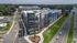 Aerial view of a modern, multi-story apartment complex with sleek architecture, large windows, and lush green surroundings, offering urban living in a vibrant neighborhood.