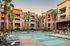 Luxurious apartment complex with a stunning swimming pool, surrounded by palm trees and modern architecture under a serene sunset.