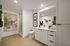 Modern bathroom oasis with sleek glass shower, elegant white cabinetry, and vibrant greenery accents, highlighted by contemporary art.