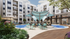 Luxurious apartment courtyard featuring a modern pool area with stylish blue sunshades, vibrant greenery, and inviting lounge seating for relaxation.