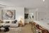 Elegant living space with modern decor features a cozy cream sofa, abstract wall art, and sleek kitchen island with chic barstools.