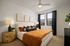 Modern bedroom featuring a luxurious bed with vibrant orange bedding, elegant side tables, and minimalist wall art, bathed in natural light from double-paned windows.