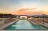 Luxurious outdoor pool with stylish lounge chairs and umbrellas set against a stunning sunset backdrop, perfect for relaxation and enjoyment.