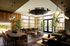 Luxurious living room featuring elegant wood paneling, modern lighting, and expansive windows with lush outdoor views. Stylish seating areas and chic dining space create a warm ambiance.