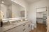 Elegant bathroom with modern double vanity, illuminated mirror, and spacious walk-in closet showcasing organized shelving and hangers.