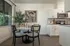 Bright dining area with elegant round table, modern chairs, and a chic kitchen corner, complemented by stylish art and lush greenery.