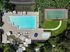 Breathtaking aerial view of a luxury apartment complex featuring a sparkling swimming pool, elegant sun loungers, a relaxing hot tub, and a vibrant tennis court set amidst lush greenery.