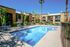North Las Vegas, NV, Apartments With In-Unit Washer and Dryer - Desert Ridge Apartments - Outdoor Swimming Pool With Lounge Chairs, Seating With Umbrella, Trees, Metal Fence, and Apartment Buildings.