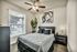 Three-Bedroom Apartments in North Austin, TX - Lotus Village Apartments - A Bedroom With Ceiling Fan, Large Window, Nightstand, And Modern Wall Art.
