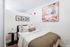 Pet-Friendly Apartments in West Oakland, CA - Prescott Station - Bedroom Features A Neatly Made Bed With White Bedding, A Brown Throw Blanket, A Side Table, Framed Photos, And Wood-Style Floors.