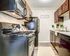 One-Bedroom Apartments in Glendale Heights, IL - Ellyn Crossing Apartments - Galley Kitchen With Dark Cabinets, Subway Tile Backsplash, Black Appliances, and Sink.