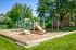 Apartments for Rent in Glendale Heights, IL - Ellyn Crossing Apartments - Outdoor Playground With Slide, Climbing Bars, Swing Set, and Mulch Area Beside Trees.