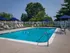 Inviting outdoor pool area with sleek lounge chairs, blue umbrellas, and lush green surroundings, perfect for relaxation and sunny days.