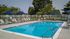 Inviting outdoor pool area with comfortable lounge chairs and vibrant blue umbrellas, surrounded by lush greenery and a pristine white fence.