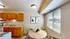 Bright and inviting kitchen with warm wooden cabinets, modern appliances, and a cozy dining area featuring stylish green chairs and a round wooden table.
