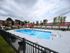 Inviting pool area with red umbrellas, lounge chairs, and a fenced patio, perfect for relaxation and entertainment at a scenic apartment community.