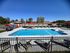 Inviting outdoor pool area with crystal clear water, surrounded by comfortable lounge chairs and vibrant red umbrellas, perfect for a relaxing day under the sun.