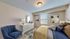 Charming bedroom with elegant decor featuring a plush blue armchair, stylish dresser, and cozy bedding accented by modern art.