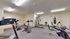 Modern fitness room featuring a variety of high-quality exercise equipment, including a treadmill, stationary bikes, and a punching bag, in a well-lit, spacious environment.