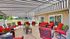 Charming outdoor patio with vibrant red cushioned seating, elegant striped awning, and lush greenery, offering a perfect space for relaxation and entertaining.