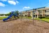 Charming residential community with modern playground, lush greenery, and serene pond backdrop.