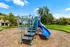 Charming community playground with modern equipment, surrounded by lush green lawns and inviting apartment homes.