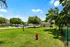 Vibrant dog park with lush green grass, agility equipment, and a bright red fire hydrant, surrounded by trees and secure fencing, under a clear blue sky.