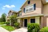 Charming two-story townhouse with well-maintained greenery, inviting front entrance, and elegant shutters, set under a clear blue sky.