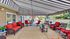 Charming outdoor patio featuring cozy red-cushioned seating, elegant striped awning, and delightful potted plants, perfect for relaxation and entertainment.