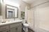 Modern bathroom featuring sleek vanity with large mirror, elegant fixtures, and a tiled shower with a sophisticated curtain.