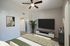 Modern bedroom with elegant decor, featuring a large flat-screen TV, stylish ceiling fan, and chic green accents.